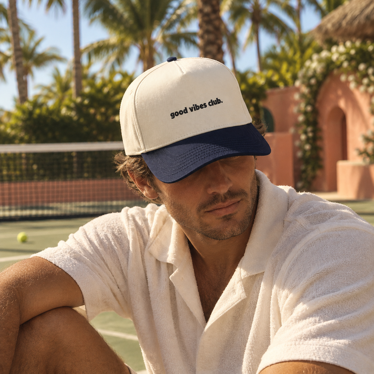Model wearing the Natural and Midnight Ronny Cap beside a tennis court.