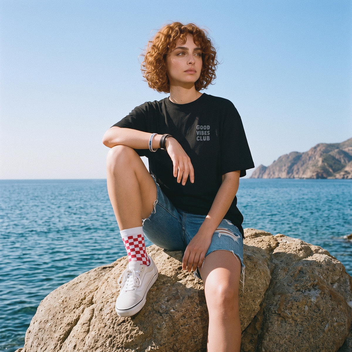 Model seated on a rock wearing the Black Oversized Club Tee.