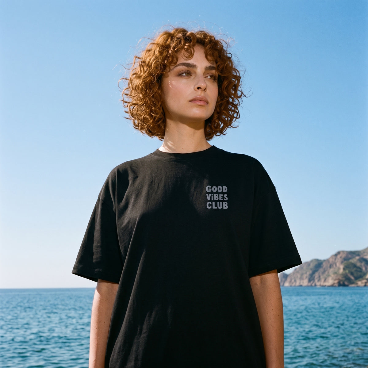 Model wearing the Black Oversized Club Tee by the coast.